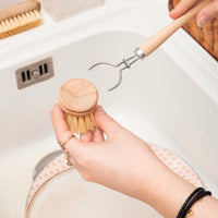 Person holding a wooden dish brush and a metal scrubber over a sink.